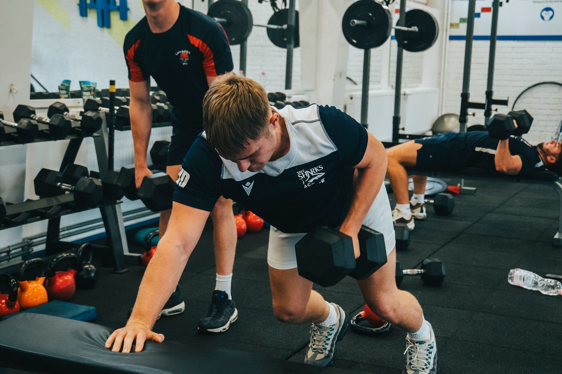 Young athletes training with dumbbells under a coach's eye